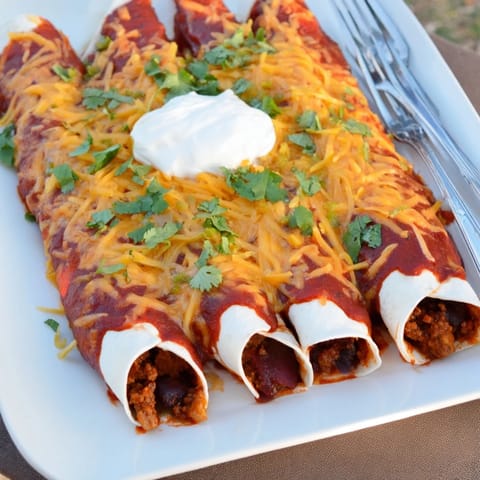 Golden baked Beef Enchiladas filled with seasoned ground beef, topped with cilantro and a dollop of sour cream.