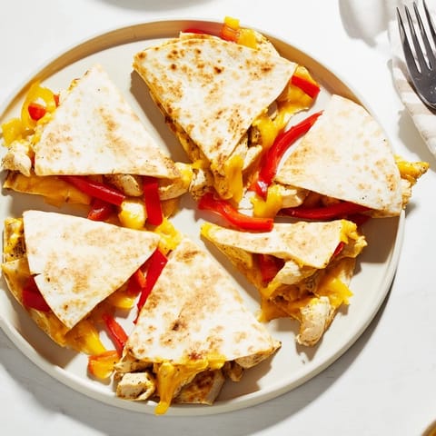 Close-up of a Chicken Quesadilla filled with grilled chicken, sautéed red bell peppers, and onions, served with a side of fresh salsa.