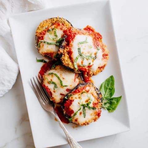 Crispy breaded Eggplant Parmesan rounds plated with fresh basil, marinara, and a side salad for a classic Italian meal.