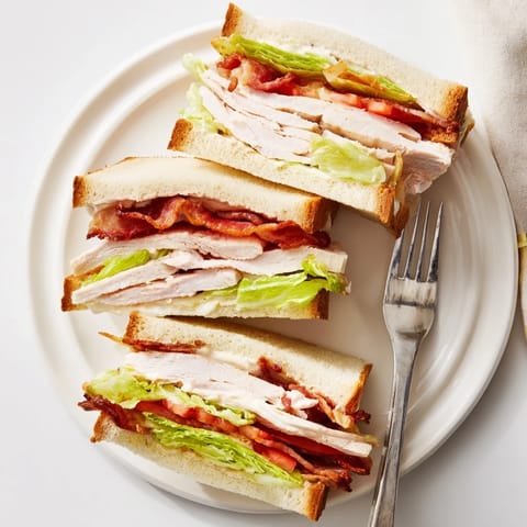 Golden toasted triple-decker Turkey Club Sandwich with crispy bacon, fresh lettuce, and tomato on a plate, served with potato chips.