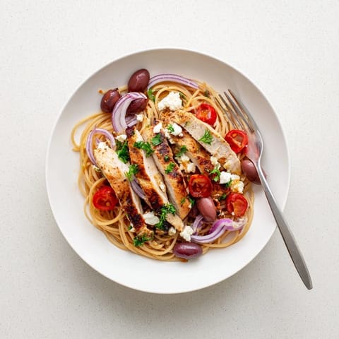 Freshly grilled chicken slices rest atop Greek Chicken Spaghetti with juicy red tomatoes and briny Kalamata olives.