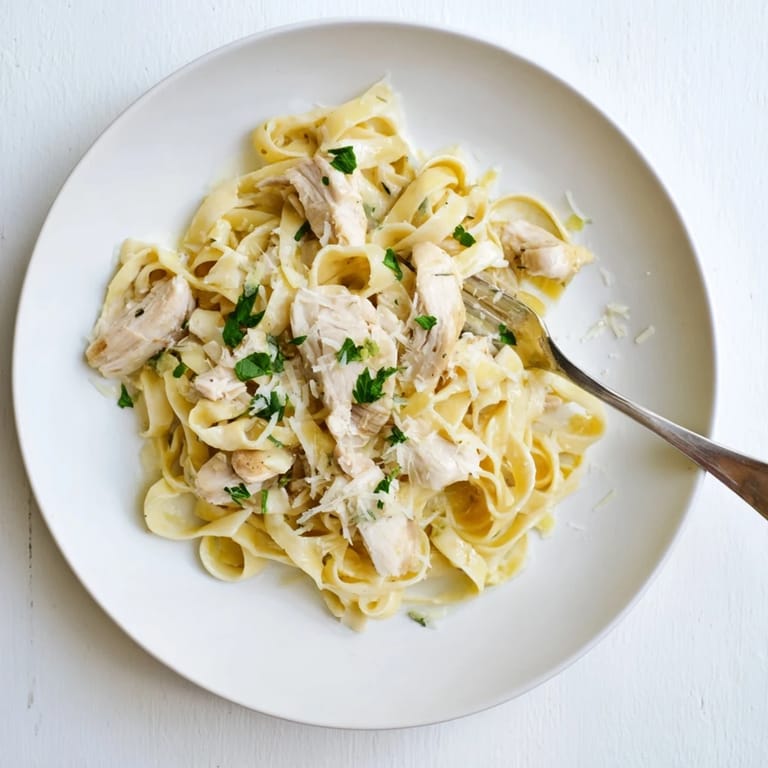Restaurant-style fettuccine Alfredo plated with fresh parsley, grated Parmesan, and a glass of white wine.