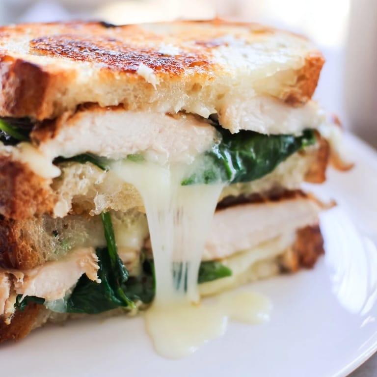 Sliced Grilled Chicken Spinach Panini showing juicy grilled chicken and melty cheese on buttery, crusty Italian bread.