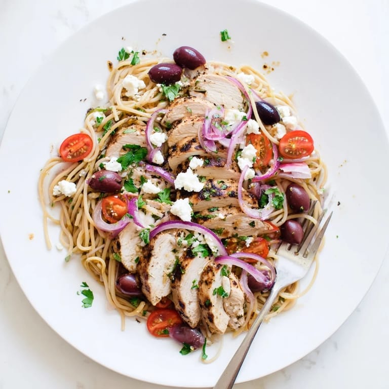 A warm bowl of Greek Chicken Spaghetti features crumbled feta, red onion, and fresh parsley garnish.