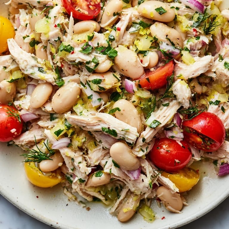 Close-up view of Lemony White Bean Chicken Salad showing juicy shredded chicken, bright red cherry tomatoes, and fresh dill mixed with white beans for a refreshing meal.