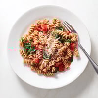 Steaming tomato spinach one-pot rotini served hot in a white bowl, garnished with fresh basil and grated Parmesan.  
