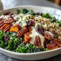 Golden roasted sweet potatoes and fluffy quinoa piled high in a Harvest Kale Quinoa Bowl, topped with toasted pecans and dried cranberries.