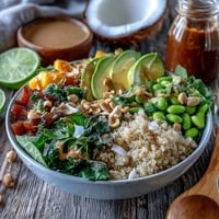 Vibrant Thai Coconut Quinoa Bowl topped with crisp red peppers, carrots, and cucumber, drizzled with creamy peanut dressing and sesame seeds.