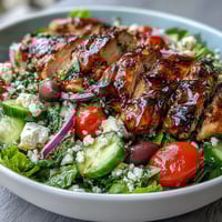 Greek Salad Bowl with Grilled Chicken, featuring juicy marinated chicken atop crisp lettuce, ripe tomatoes, and tangy feta, drizzled with a zesty dressing.